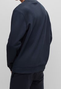 Sudadera de color azul marino hecha de una suave mezcla de algodón, con cuello redondo, puños y dobladillo de canalé, y un diseño minimalista.