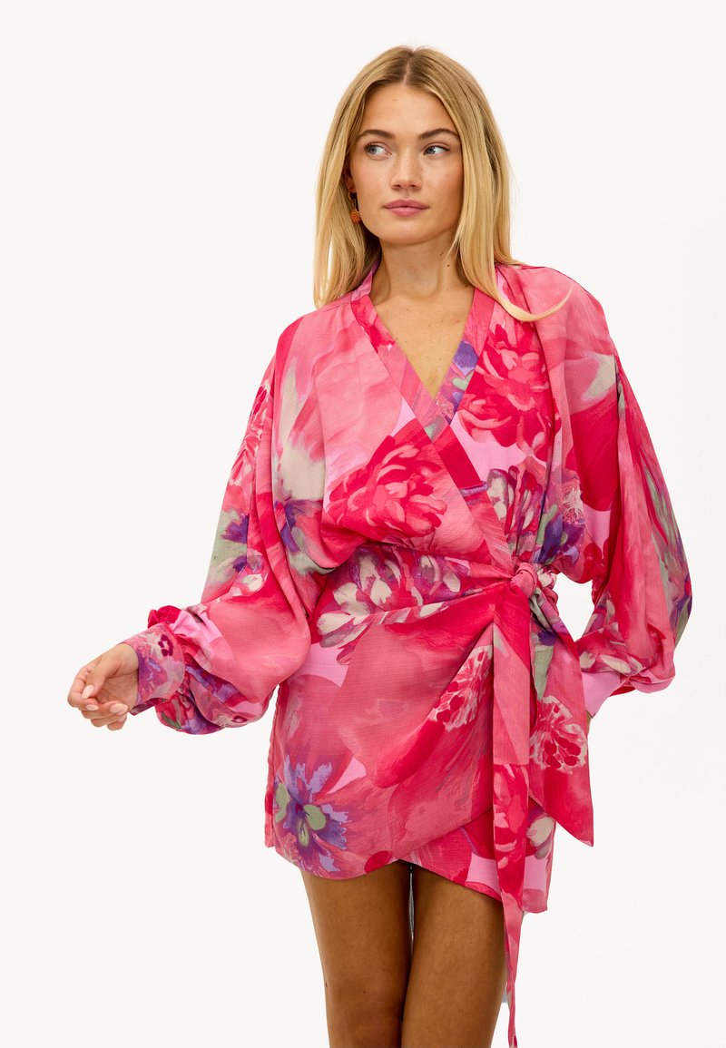 Robe portefeuille florale rose avec de longues manches volumineuses, décolleté en V et taille à nouer. Tissu léger et transparent avec un motif floral éclatant.