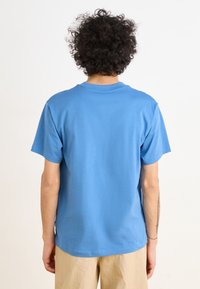 Modré bavlněné tričko s krátkými rukávy a kulatým výstřihem, zobrazené zezadu. Vyznačuje se hladkou texturou a volným střihem.