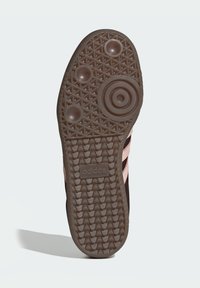 Suela de zapato de goma marrón oscuro con un patrón intrincado, tres acentos rosas, logo y elementos circulares de tracción.