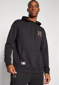 Melna kapuce ar kangaroo kabatu, ar metālisku logotipu uz krūšu un MLB emblēmu uz apakšmalas. Mīksts audums ar ribotiem piedurknēm.