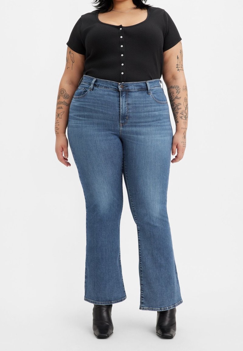 Svart randig kortärmad topp med knappstängning, tillsammans med utsvängda blå denimjeans. Betonar hög midja och subtil blekning. Svarta anklarboots.