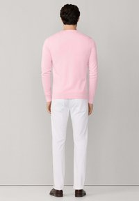 Maglione aderente da uomo in cotone rosa chiaro, con maniche lunghe e scollo rotondo. Abbinato a pantaloni bianchi e scarpe marroni. Vista posteriore.