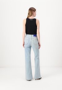 Svart ermeløs topp og lyseblå høy midje, flagrende jeans. Stoffet ser ut som bomull, med et synlig logo på baksiden av midjebåndet.