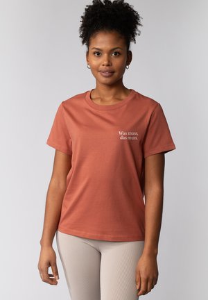 Rustkleurig T-shirt van katoen, met korte mouwen en een ronde hals. Er staat witte tekst op de voorkant: "Was muss, das muss."
