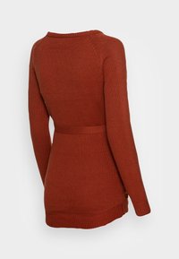 Långärmad, ribbad tröja i rödbrun färg med en bred rund halsringning och en åtsittande midja. Har sidslitsar och texturerade detaljer på ärmarna.