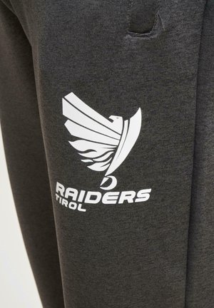 Ciemnoszare spodnie dresowe z białym logo stylizowanego ptaka oraz napisem "RAIDERS TIROL" nadrukowanym na lewej udzie. Miękki w dotyku materiał.
