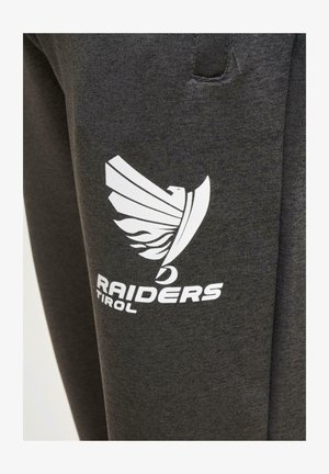 Ciemnoszare spodnie dresowe z białym logo stylizowanego ptaka oraz napisem "RAIDERS TIROL" nadrukowanym na lewej udzie. Miękki w dotyku materiał.