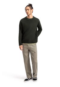 Felpa a maniche lunghe di un verde scuro con una vestibilità rilassata, dotata di maniche raglan. Abbinata a pantaloni cargo beige chiaro e sneakers nere.