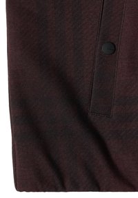 Tissu brun foncé avec un rabat rectangulaire cousu et un seul bouton rond noir sur le côté droit.