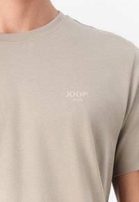 Beige cotton t-shirt with a crew neck, featuring a small white "JOOP! JEANS" logo on the left chest area. Smooth texture.