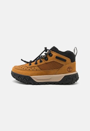 Bruin suede en mesh wandelschoen met zwarte accenten, rubberen zool en vetersluiting. Bevat perforaties voor ademend vermogen en een logo.