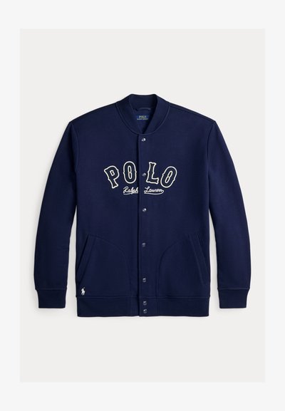 Μπουφάν σε ναυτικό μπλε χρώμα με κουμπιά και κείμενο "POLO Ralph Lauren" στο στήθος, δύο μπροστινές τσέπες, ριμπ κολάρο και μανσέτες, και μικρό λογότυπο κοντά στο τελείωμα.