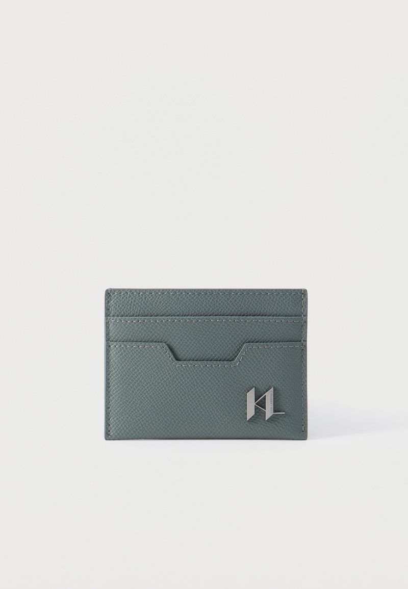 Λεπτός γκρι δερμάτινος θήκη καρτών με υφή επιφάνειας, πολλαπλές θήκες για κάρτες και μικρό μεταλλικό λογότυπο στην κάτω δεξιά γωνία μπροστά.