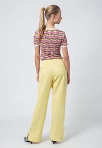 Camisa de punto con patrón de zigzag multicolor combinada con pantalones amarillos de tiro alto y pierna ancha que tienen aberturas laterales y bolsillos.