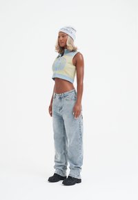 Uppskuren, ärmlös grön och blå topp som matchas med ljusblå denimjeans med sidgrafik. Accessoarer inkluderar en grå mössa och svarta skor.