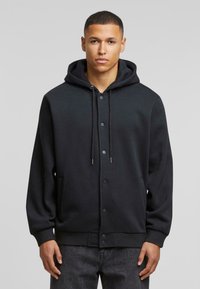 Zwarte hooded sweatshirt met een knoopsluiting aan de voorkant, trekkoorden en zijzakken. Zacht materiaal met een losse pasvorm en geribde manchetten.