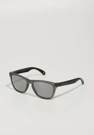 Czarne okulary przeciwsłoneczne mają szary, teksturowany korpus z wzorzystym wzorem. Soczewki są ciemne i prostokątne, z logo Oakley po boku.