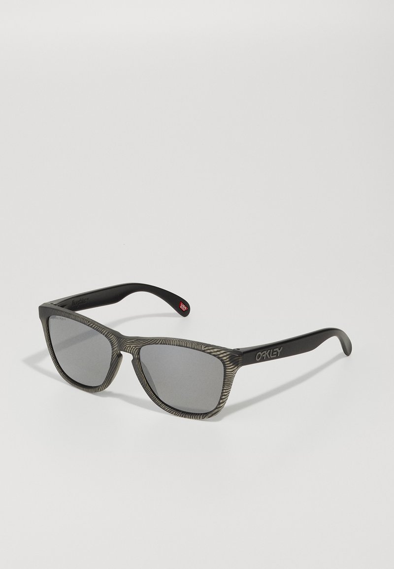 Ochelarii de soare negri au un cadru gri texturat cu un design modelat. Lentilele sunt întunecate și de formă rectangulară, având logo-ul Oakley pe lateral.