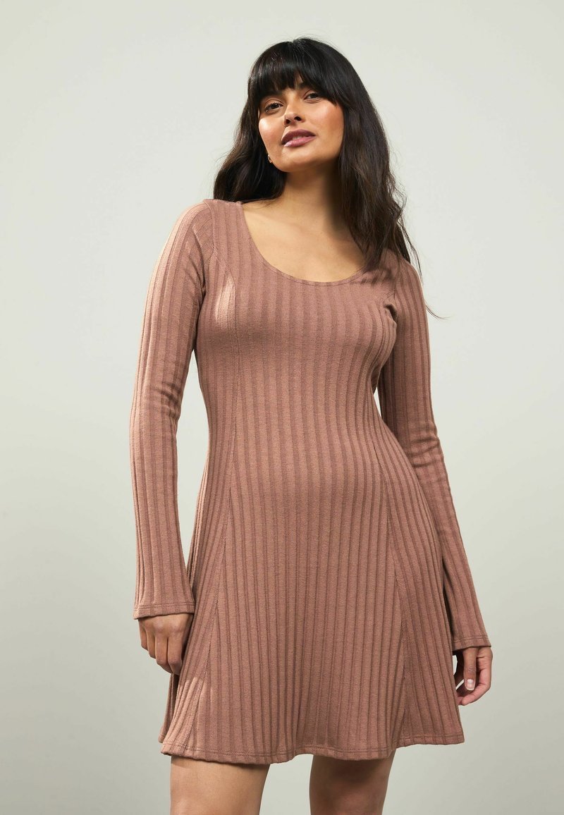 Ribbade långärmade klänning i dämpad rosa, med en rundad halsringning, åtsittande bodice och en flödande kjol som mjukt vidgar sig nertill.