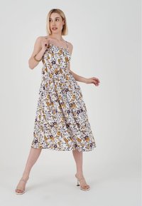Bloemen midi-jurk met witte achtergrond, versierd met paarse en gele bloemen, dunne banden, gerimpelde taille en een vloeiende rok. Gladde stofstructuur.