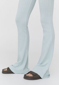 Pantalon évasé côtelé bleu clair avec une texture lisse, associé à des sandales marron avec une large bride et une fermeture Velcro ajustable.