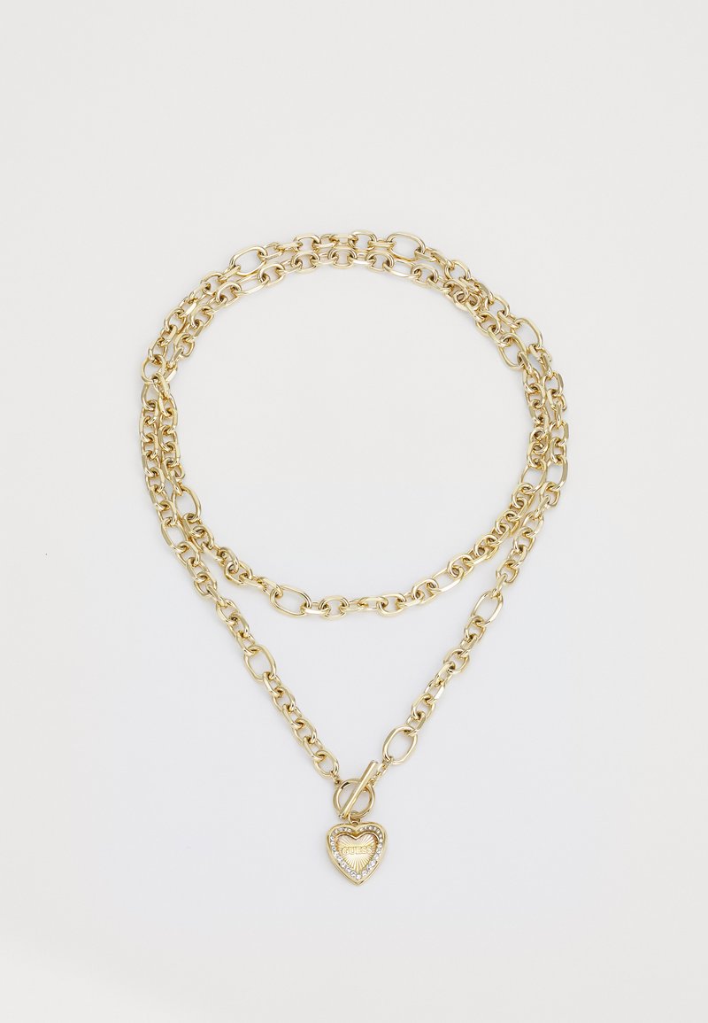 Collana a più strati in tonalità oro, caratterizzata da anelli allungati e rotondi, con un pendente a forma di cuore accentuato da piccole pietre trasparenti.