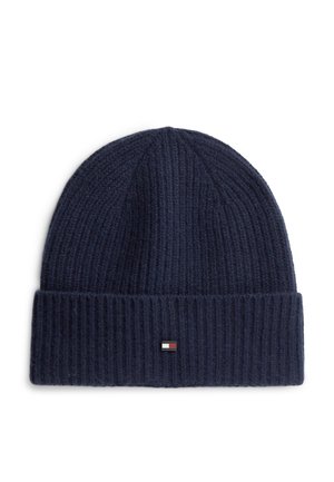 Marineblaue gerippte Strickmütze mit umgeschlagenem Bündchen und kleinem rechteckigem roten, weißen und schwarzen Logoaufnäher vorne in der Mitte.