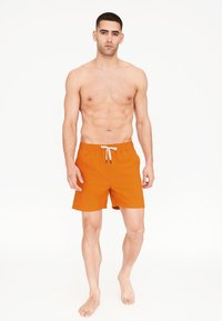 Oranžové plavkové šortky z lehkého materiálu s elastickým pasem a bílým šňůrkem na stažení. Délka do poloviny stehna s hladkým povrchem.