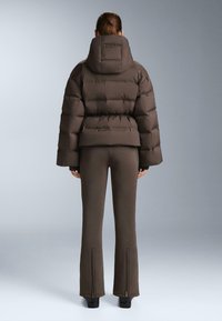 Hnedá páperová bunda s vysokým golierom a širokými rukávmi, doplnená o zodpovedajúce priliehavé nohavice s zipsovými akcentami na okrajoch.