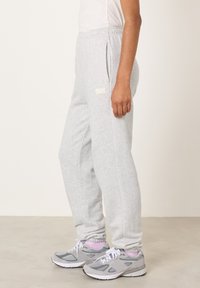 Sivé tepláky z mäkkej tkaniny s bočnými vreckami a elastickým pásom, s malým logom umiestneným na ľavom stehne.