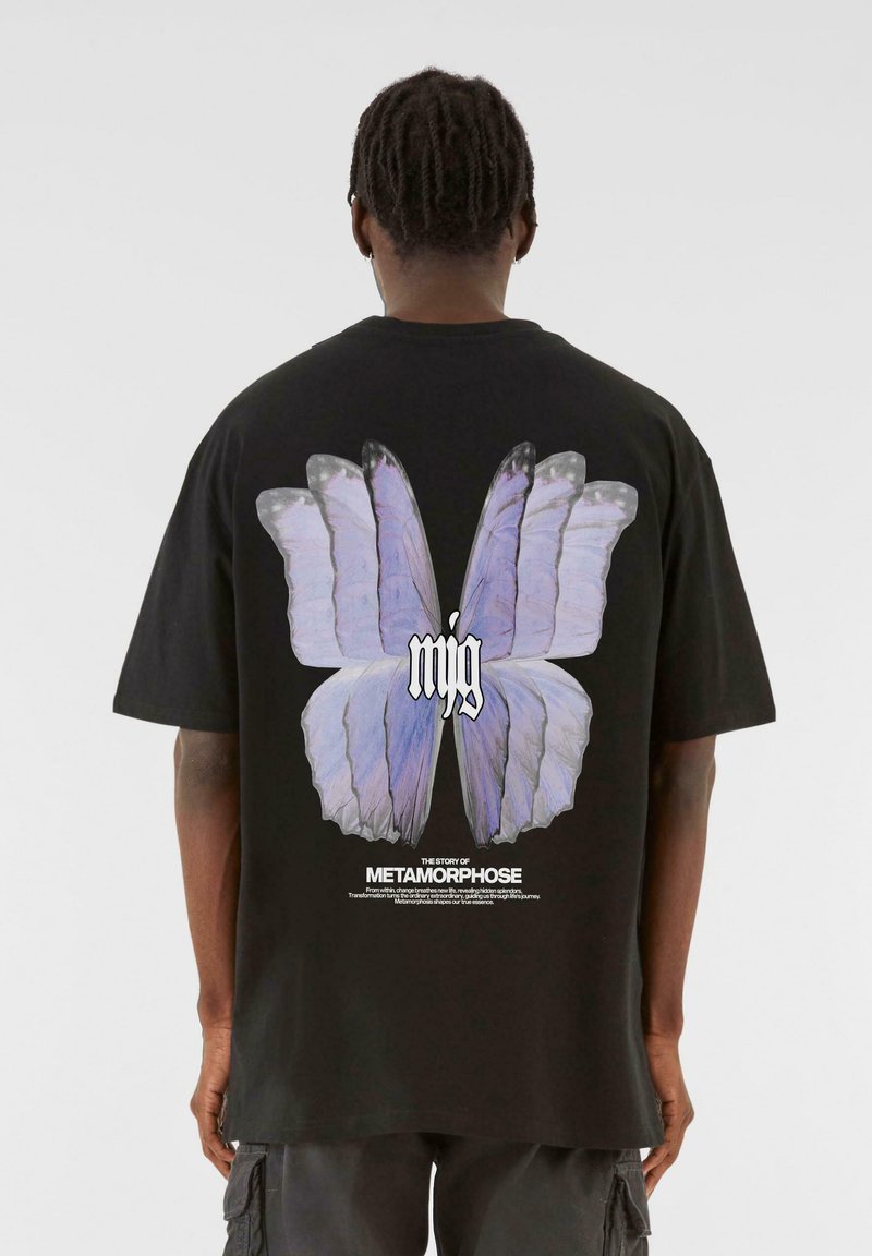 Sort bomulds t-shirt med et stort sommerfuglegrafik i lys lilla på ryggen, med hvid tekst underneath. Korte ærmer og afslappet pasform.