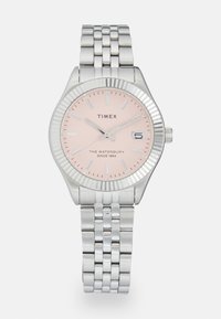 Montre en acier inoxydable argenté avec un cadran rose clair, une fenêtre de date à 3 heures et une lunette texturée. Elle est dotée d'un bracelet à maillons.