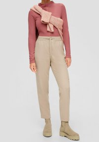 Sopiva vaaleanpunainen pitkähihaisesti paita korkealla kauluksella, yhdistettynä beigekoristeisiin kapeisiin housuihin. Neulottu vaaleanpunainen huivi roikkuu rentona hartioilla.