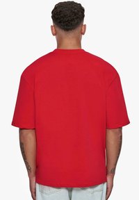 Camiseta de algodón roja con mangas cortas y corte relajado. Presenta un escote redondo y un diseño minimalista, vista desde la espalda.