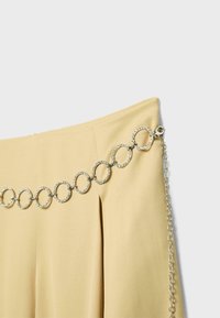 Světlé béžové sukně se stříbrným řetízkovým pásem s texturovanými kruhovými články a zapínáním na pravé straně.