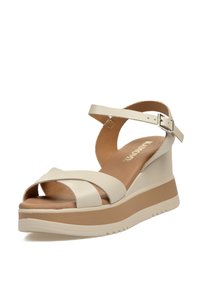 Sandalia cuña de color beige claro con dos tiras cruzadas, correa para el tobillo con hebilla y una plantilla acolchada. Presenta una suela texturizada.