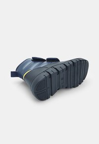 Granatowe wodoodporne buty z gładkiej skórzanej cholewki, żółtym akcentem i teksturowaną czarną gumową podeszwą z głębokimi rowkami dla lepszej przyczepności.