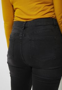 Vaqueros negros de talle alto con una textura suave, que cuentan con dos bolsillos traseros y detalles sutiles de desgaste cerca del borde de uno de los bolsillos.