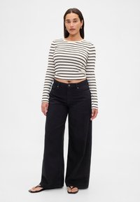 Svarta vida jeans kombinerade med en kort, svartvit randig långärmad topp. Tyget är mjukt med en slät textur.