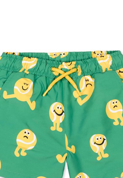 Shorts verts ornés de personnages de balles de tennis jaunes affichant diverses expressions faciales et poses, avec un cordon jaune à la taille élastique.