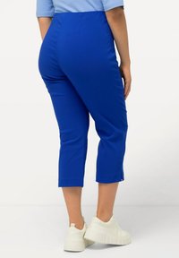 Pantaloni capri blu con un tessuto liscio, design aderente e spacchi ai lati dell'orlo, abbinati a sneakers bianche. Adatti per un look casual.