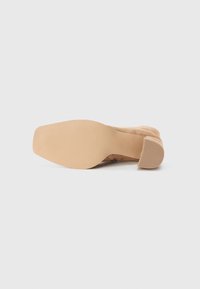 Nude suede high-heeled shoe featuring a rounded toe and a textured beige rubber sole with a block heel for stability.