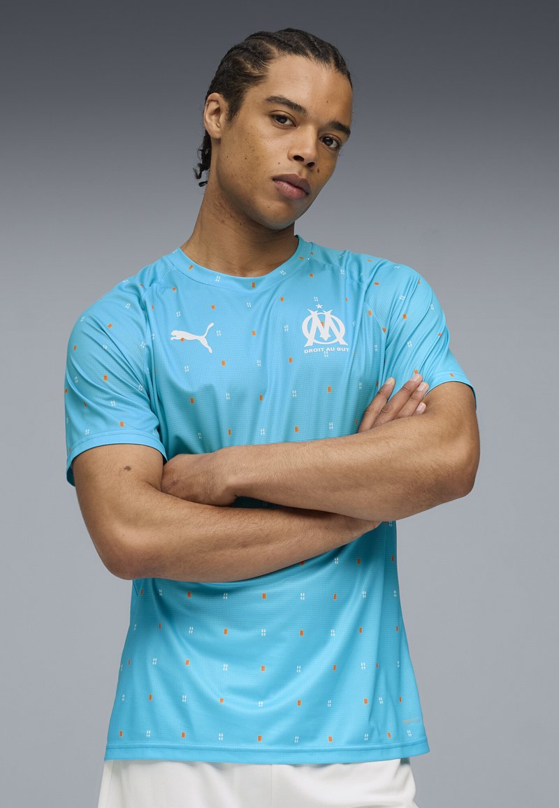 Gai zilas sporta krekls ar apelsīnu un baltām kvadrātu līnijām, kuram ir Puma logo un Marseļas kluba emblēma. Īsām piedurknēm, ar apaļu kakla izgriezumu.