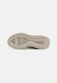 Világos bézs szövetű sneaker talp, barázdált textúrával, amelyen barázdák találhatók a tapadás érdekében, és egy logó van bélyegezve a külső oldalán.