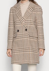 Cappotto doppiopetto in un motivo a quadri beige e marrone. Presenta ampie revers, due tasche frontali e bottoni neri. Tessuto morbido e texturizzato.
