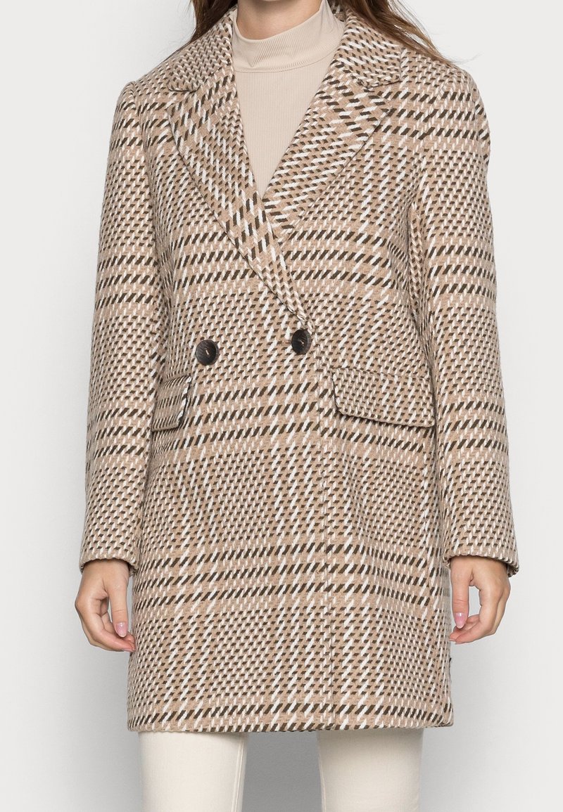 Cappotto doppiopetto in un motivo a quadri beige e marrone. Presenta ampie revers, due tasche frontali e bottoni neri. Tessuto morbido e texturizzato.