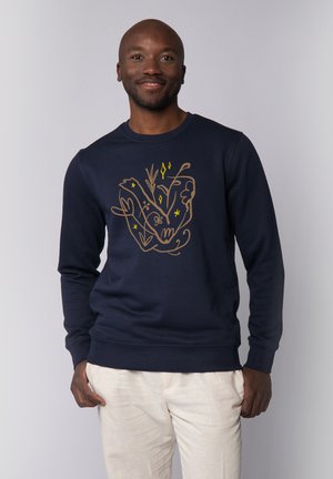 Marineblaues Crewneck-Sweatshirt mit einem goldenen und gelben illustrierten Design. Hergestellt aus einem weichen Stoff mit gerippten Bündchen und Saum.