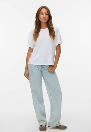 T-shirt bianco a maniche corte abbinato a jeans larghi di un leggero blu e sneaker marroni, con un fit rilassato e una tessitura di tessuto morbido.