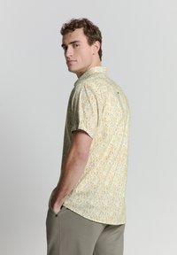 Kurzarm-Hemd in hellgelbem Stoff mit einem gemusterten Design. Verfügt über eine lässige Passform und einen einzelnen Knopfverschluss am Hals.